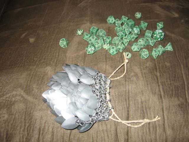 The scalemaille dicebag, opened with all of the green dice spilled beside it, on the brown couch.