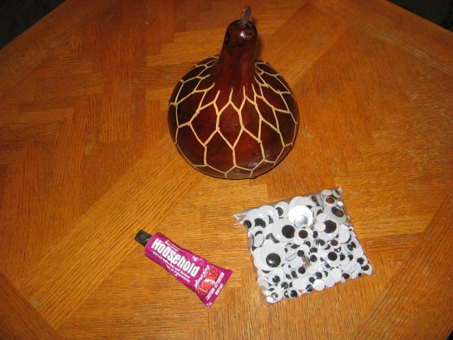A decorative gourd, with a bag of googly eyes and a bottle of glue beside it.