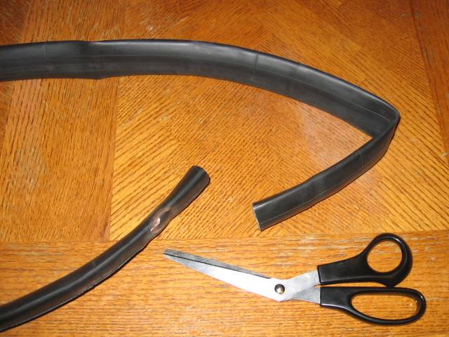 A rubber bicycle inner tube cut with scissors, sitting on a wooden table.
