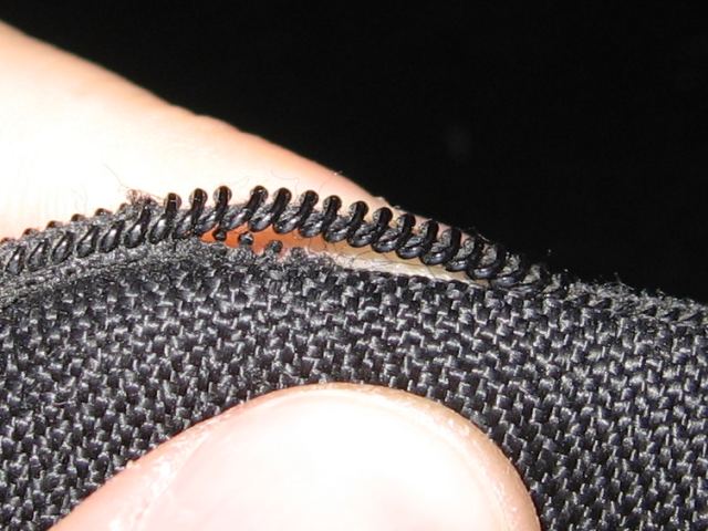 A section of black plastic zipper pulled away from the rest of the fabric.