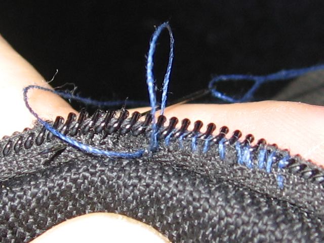 Showing a closeup of the zipper, and thread being sewn between each tooth.