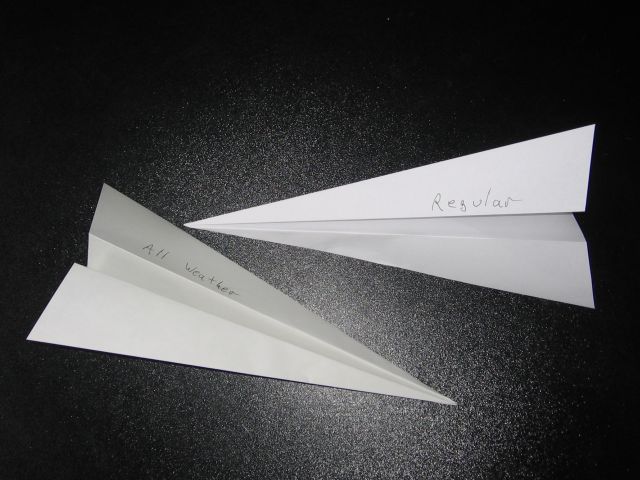 Two paper airplanes beside eachother, on a black tabletop.