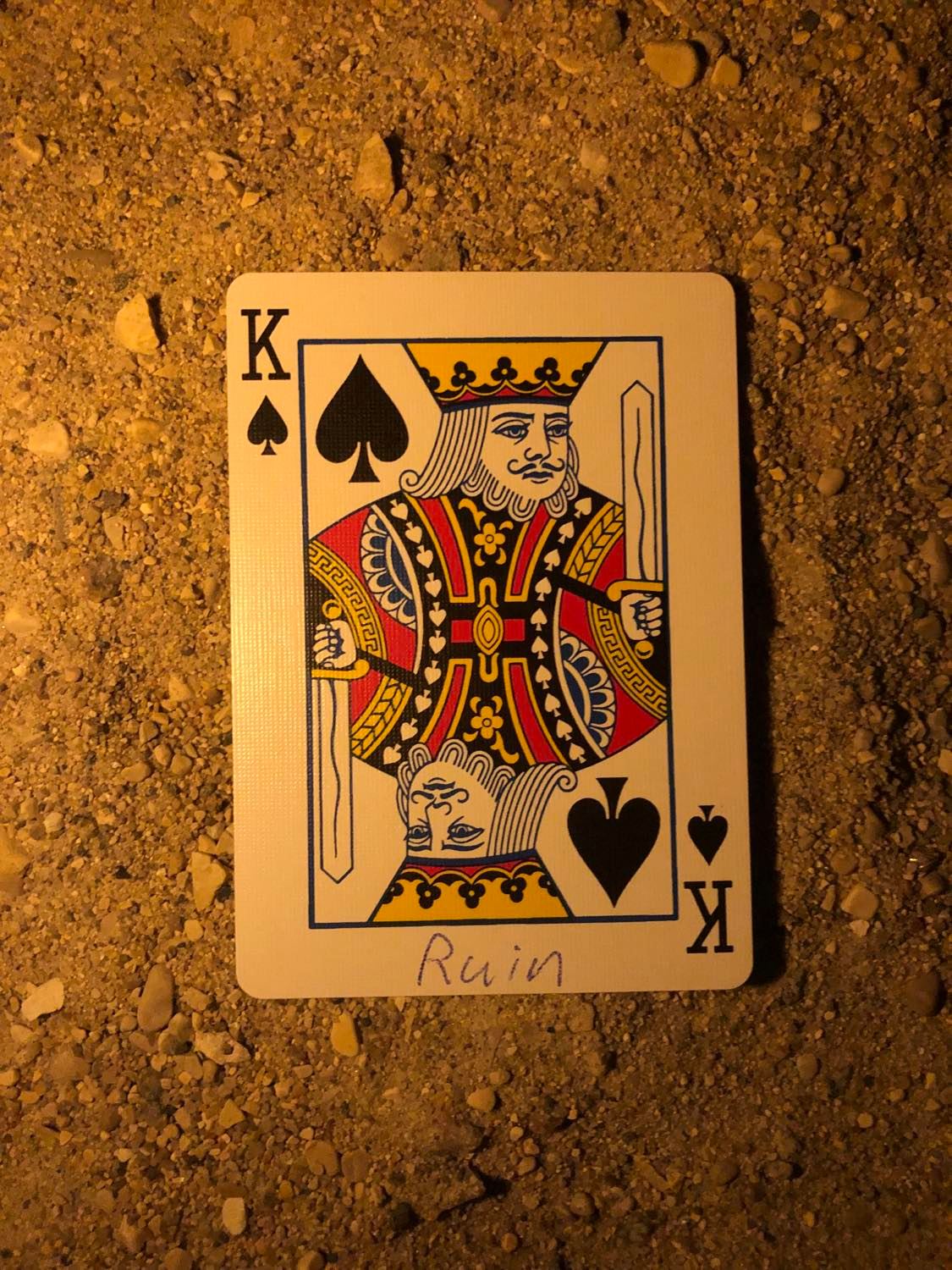 The king of spades with Ruin written on it, laying on the darkened soil.
