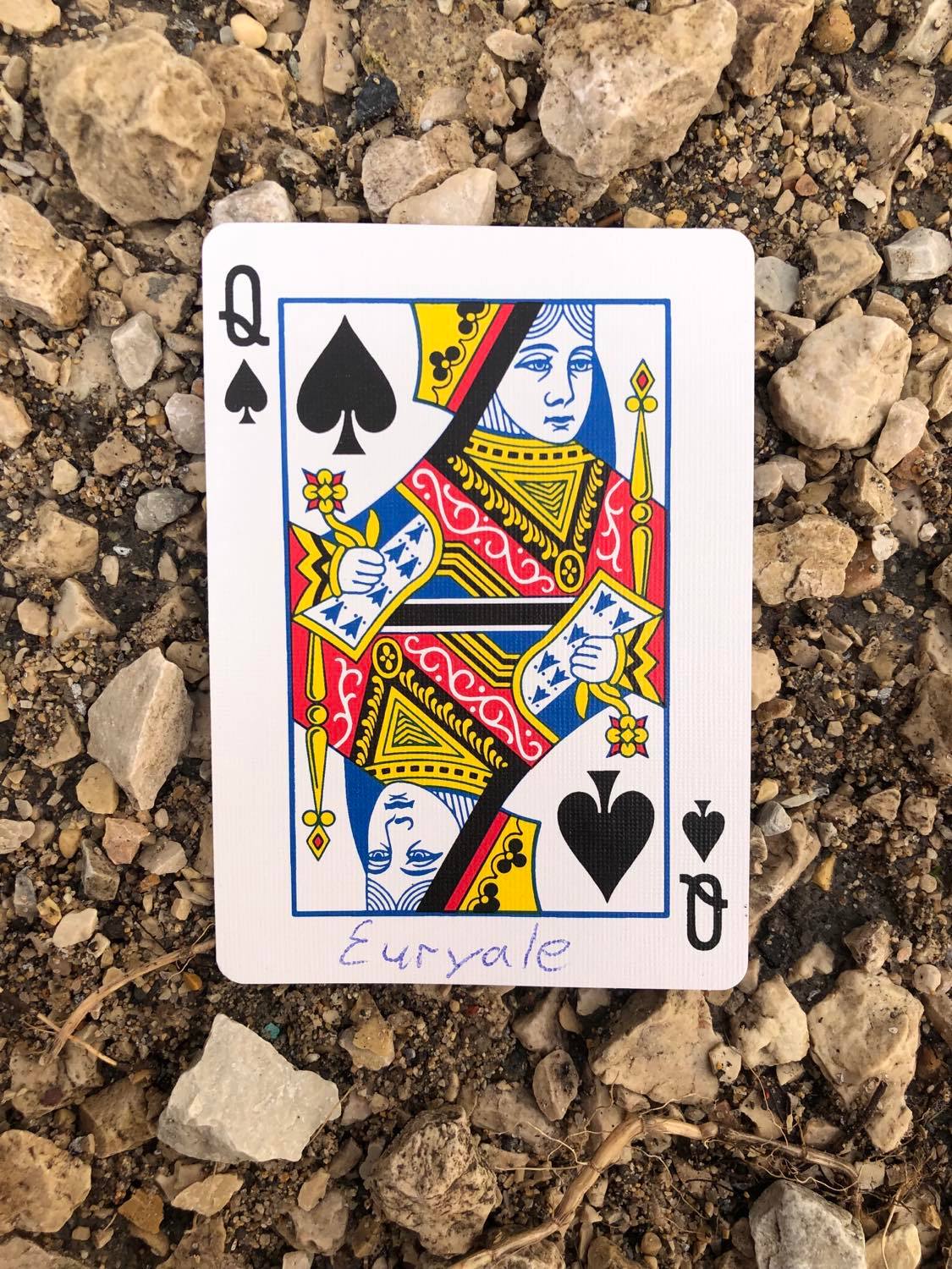 The queen of spades with Euryale written on it, laying on the gravel path.
