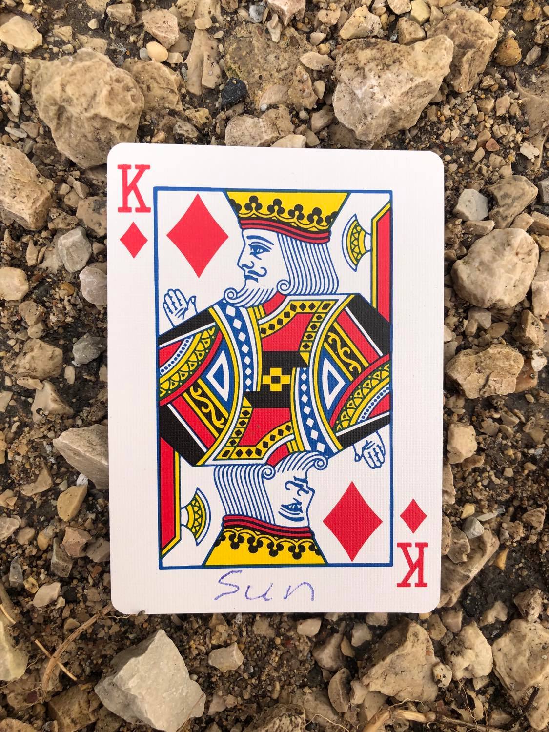 The king of diamonds with Sun written on it, laying on the gravel path.
