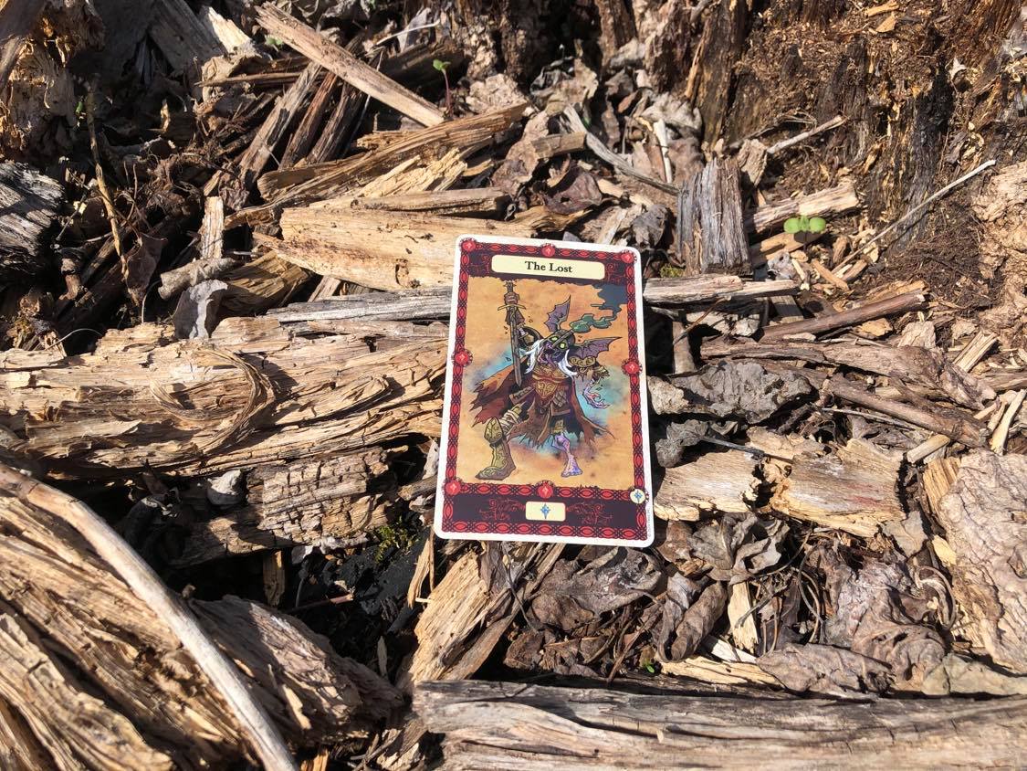 A person decaying in agony, the card laying on the forest debris.