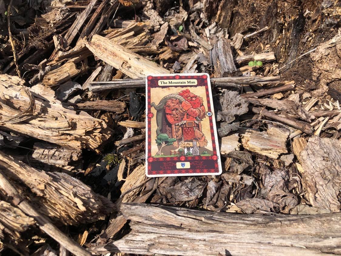 An enormous man, the card laying on the forest debris.
