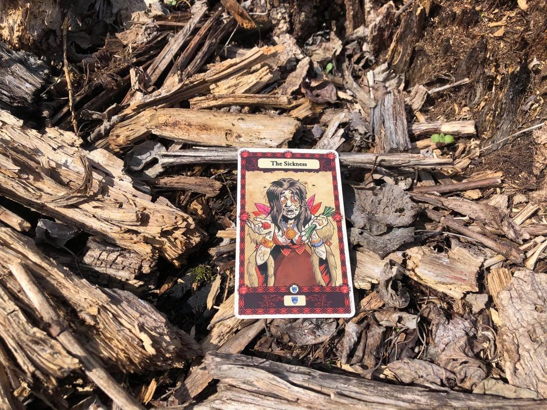 A horribly diseased woman, the card laying on the forest debris.