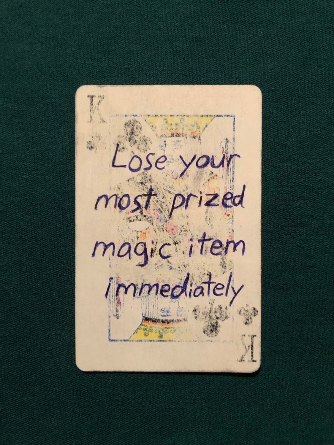 The king of clubs, laying on a green fabric.