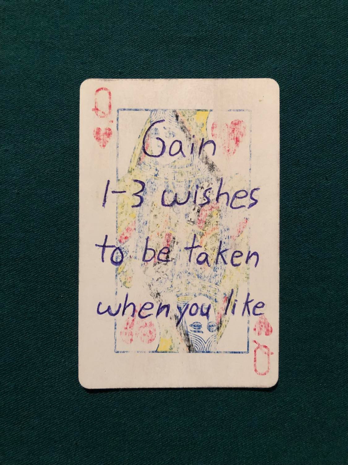 The queen of hearts, laying on a green fabric.