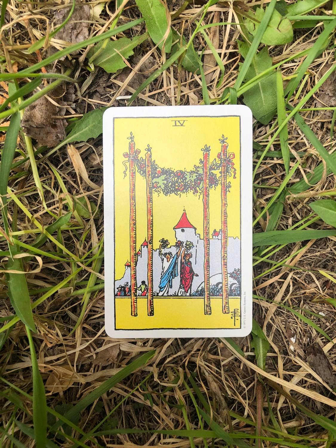 The Four of Wands, upright, laying in the grass.