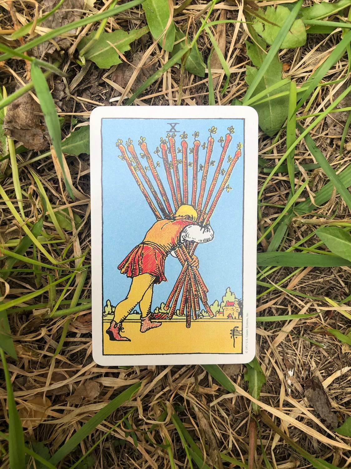 The Ten of Wands, upright, laying in the grass.