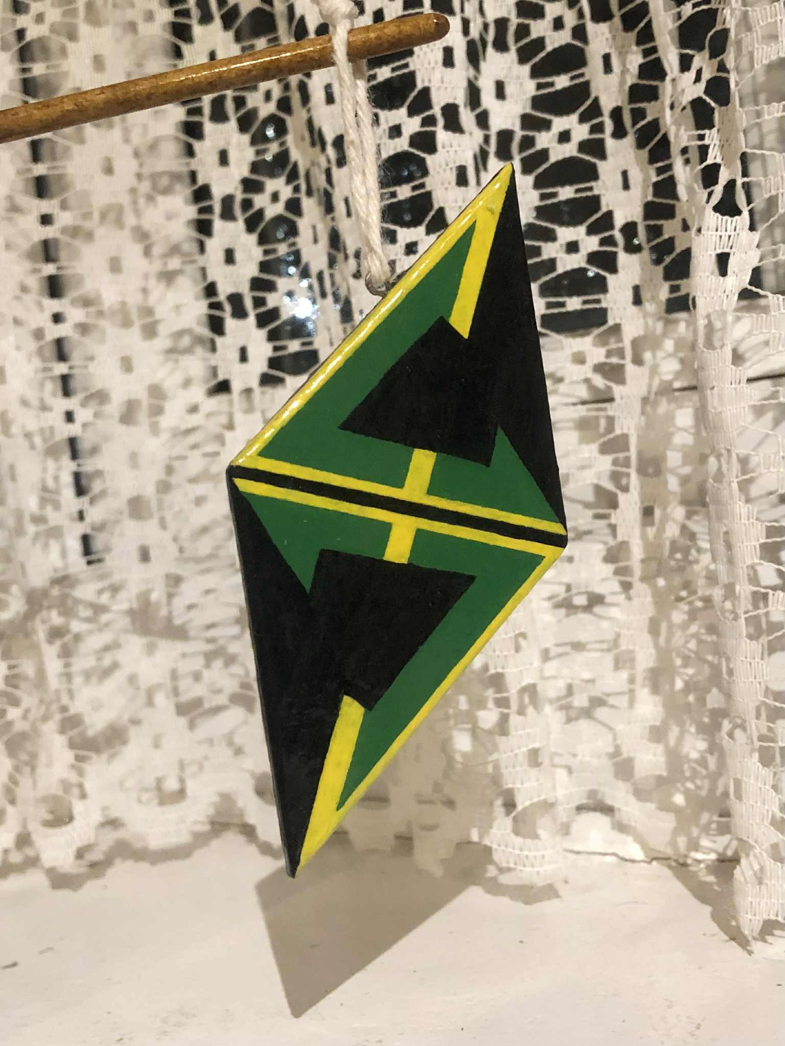 A green and yellow logo that resembles an angular letter S, on a diamond shaped plate, dangling in front of a window. The Team Sky logo.