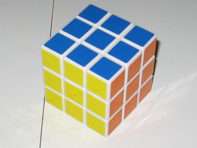 The cube with stickers applied, sitting on and reflecting off the table. Blue yellow and orange are showing.