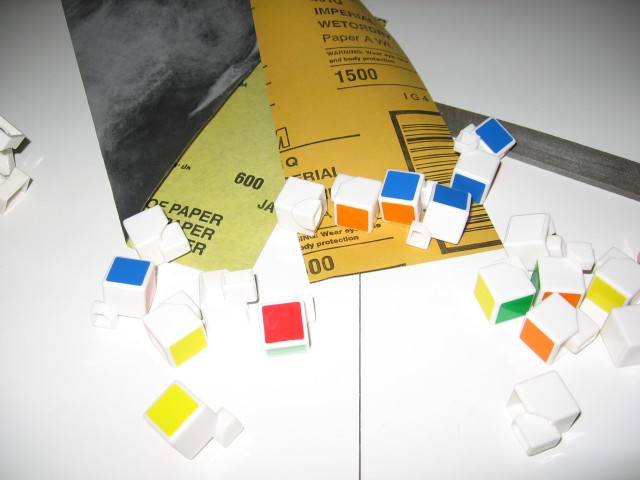 The pieces, with stickers attached, disassembled and spread out, with 600 and 1500 grit sandpaper nearby.