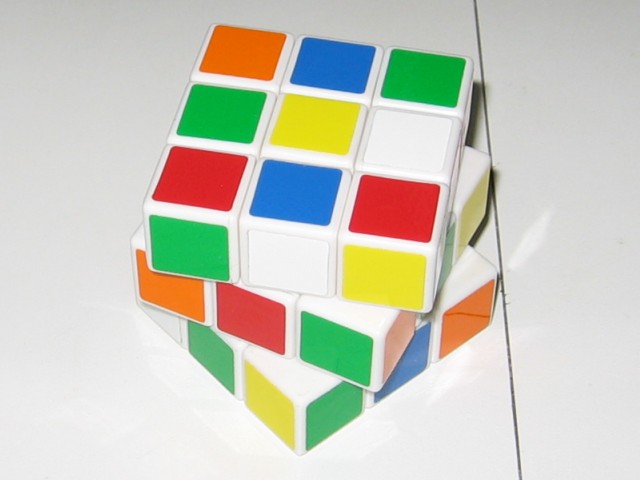 The cube put together and scrambled, each layer rotated slightly once again. Lots of greens are showing, a few yellows, a few oranges, are the most colours.