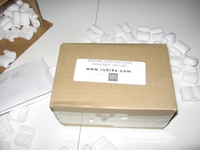The inner box outside of the outer one, sitting on the table, proudly proclaiming www.rubiks.com