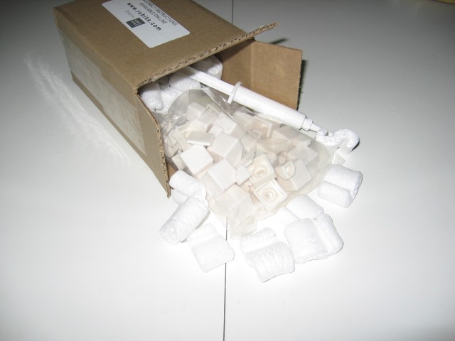 The inner box opened, holding a bag with plastic white pieces, a tube of lubricant, and more packing peanuts.