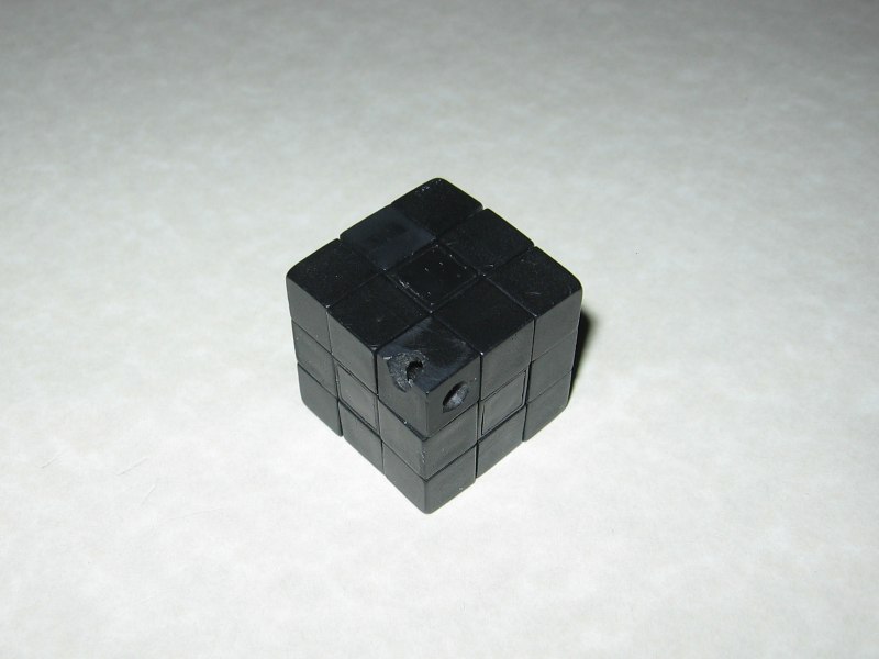 A mini Rubik's cube, with no stickers, and the chain removed from the corner, sitting on a countertop.