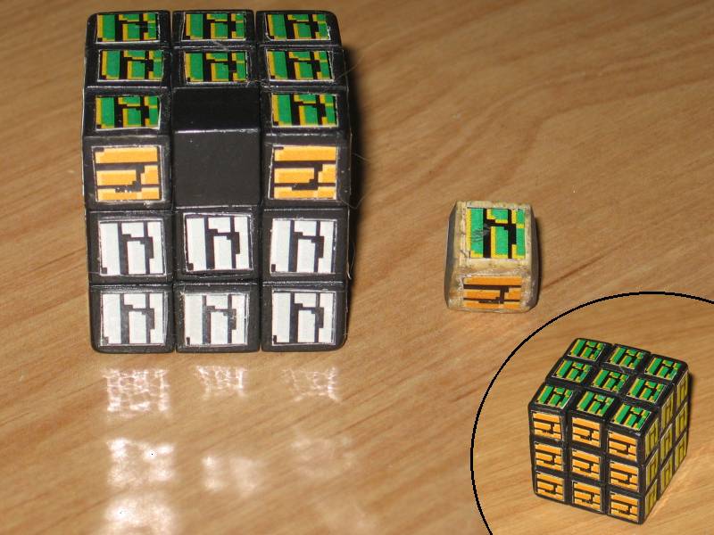 The mini Rubik's cube, showing the plastic piece in place of the wooden one, with an inset photo of the cube with stickers on all pieces.