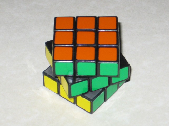 The cube reassembled, with the stickers cleaned up, and slightly rotated on each layer. The colours orange, yellow, and green are showing.