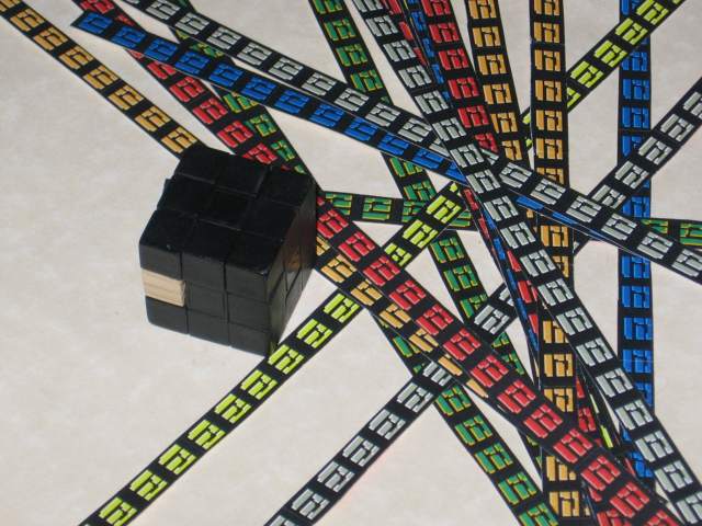 The rows of coloured floor tiles cut out from the sticker paper, scattered artistically beside the unstickered cubie.