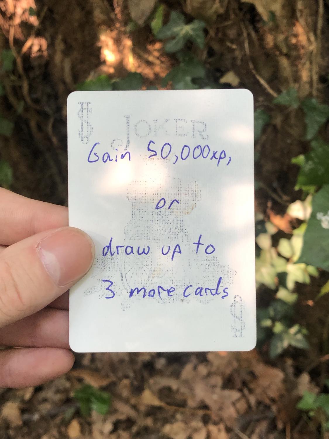 The coloured joker, held above the detritus on the ground. Gain 50,000 xp, or draw up to 3 more cards.